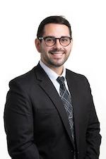 Shane Lewis posing for a professional headshot wearing a black suit and tie